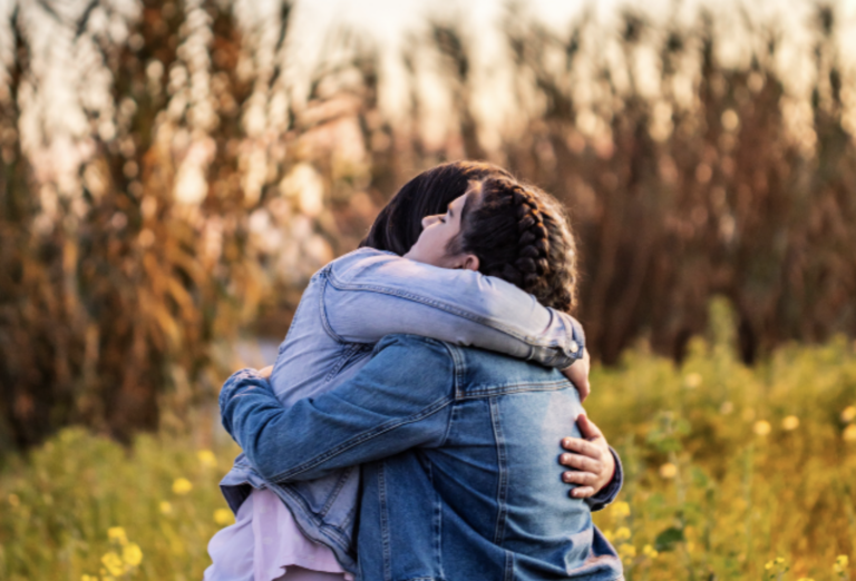 People in Jean jackets hugging in the park in fall.
